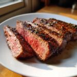 Close-up of perfectly cooked Alton Brown London broil, sliced and served on a white plate, showing a pink, juicy interior.