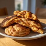 A stack of warm apple pie cookies, one broken open to reveal a gooey apple filling and cinnamon spice.