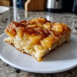 A close-up of a slice of Apple Snickerdoodle Dump Cake on a white plate, showing the moist cake and gooey apple topping.
