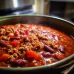 Close-up of a steaming bowl of hearty chili with ground beef, kidney beans, and diced tomatoes.