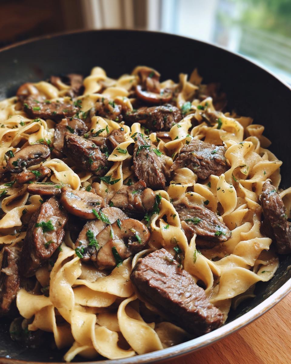 A close-up view of a pan filled with creamy Beef Stroganoff, featuring tender beef strips, mushrooms, and egg noodles, garnished with parsley.