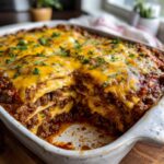 A close-up of a hearty beef taco casserole, layered with tortillas, seasoned ground beef, and melted cheddar cheese, garnished with fresh parsley.