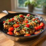 A cast iron skillet filled with juicy Bruschetta chicken topped with fresh tomatoes and basil.