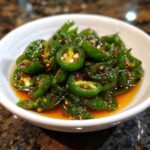 Close-up of glistening candied jalapenos in a sweet syrup, showcasing their vibrant green color and seeds.