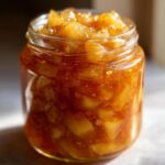 A close-up of a glass jar filled with chunky pear preserves, showing the texture and color of the preserve.