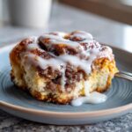 A close-up of a slice of cinnamon roll casserole on a plate, drizzled with white icing.
