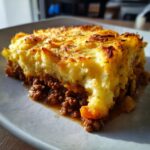A close-up shot of a hearty slice of classic shepherd's pie with a golden-brown mashed potato topping.