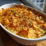 A close-up of a classic tuna casserole in a white baking dish, topped with golden-brown crispy potato chips and herbs.