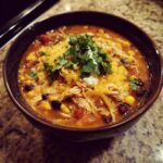 A hearty bowl of Crockpot Chicken Enchilada Soup topped with shredded cheese, sour cream, and cilantro.