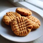 A close-up of four Easy Peanut Butter Cookies with classic fork marks on a white plate, ready to be enjoyed.