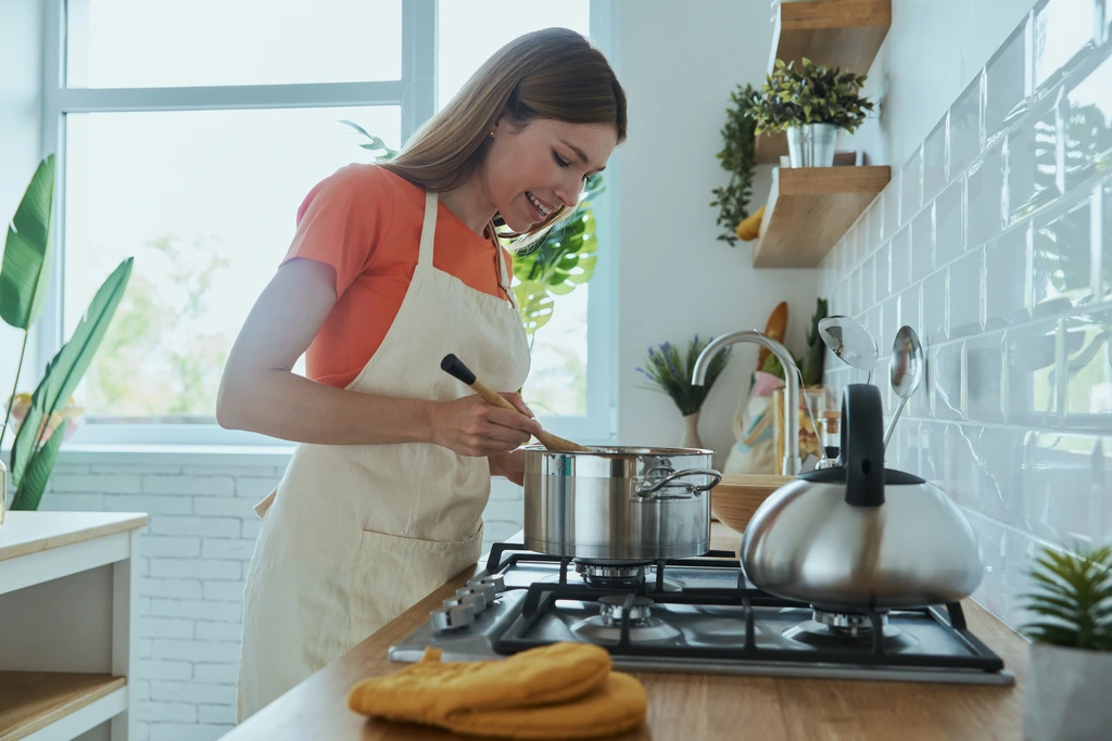 Ellie Vance smiling as she stirs a pot on the stove, happily preparing one of her easy and delicious recipes for DeliceRecipe.