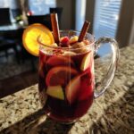 A pitcher filled with refreshing fall sangria, featuring slices of oranges, apples, and cinnamon sticks.