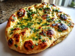 Close-up of a golden-brown garlic naan bread topped with melted butter and chopped fresh cilantro.