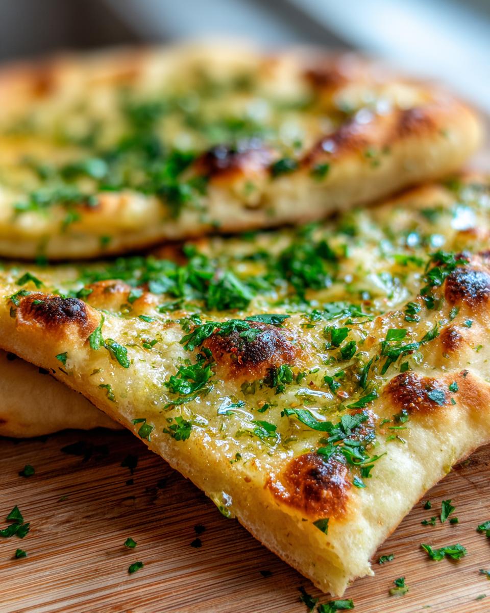 Close-up of freshly baked garlic naan bread topped with melted butter and chopped parsley.