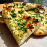 A close-up of a slice of homemade garlic naan bread, topped with melted butter and fresh parsley.