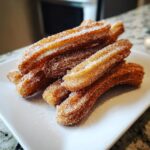 A close-up of a stack of golden brown churros coated in cinnamon sugar, ready to be enjoyed.