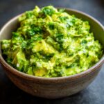 Close-up of a bowl filled with chunky, fresh Homemade Guacamole topped with chopped cilantro.