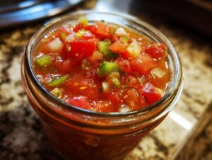 Close-up of a glass jar filled with vibrant, fresh homemade salsa, showing diced tomatoes, onions, and jalapeños.