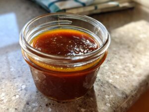Close-up of a small glass jar filled with glistening, rich brown honey BBQ sauce.