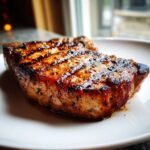 Close-up of a perfectly grilled pork chop, showcasing its juicy texture and grill marks, made with a flavorful marinade.
