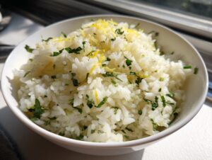 A close-up of a white bowl filled with fluffy Mediterranean lemon rice, garnished with fresh parsley and lemon zest.