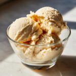 A clear glass bowl filled with creamy scoops of protein ice cream, bathed in natural light.