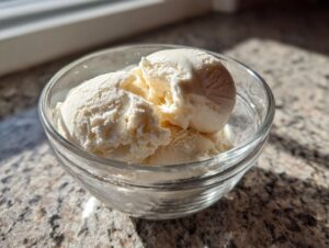 A close-up of creamy protein ice cream scooped into a glass bowl, bathed in natural light.