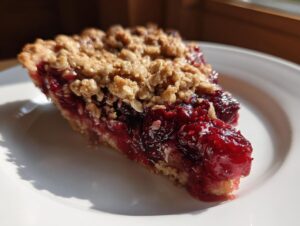 A close-up of a slice of sour cherry crisp on a white plate, showing the flaky crust and juicy cherry filling.