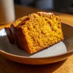 Two moist slices of sourdough pumpkin bread on a rustic plate, showcasing its vibrant orange color and tender crumb.