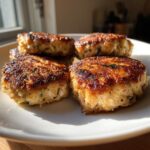 Close-up of golden brown tuna patties with visible herbs, served on a white plate.