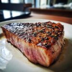 A thick, juicy tuna steak, seared and coated in a flavorful marinade, resting on a white plate.