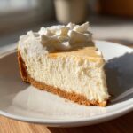 A delicious slice of 3 ingredient no bake cheesecake on a white plate, topped with whipped cream and a drizzle of sauce.