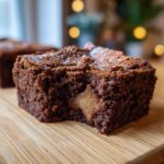 A close-up of a rich chocolate apple brownie with a bite taken out, revealing a soft apple filling.