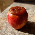 A whole red apple with a dollop of rich, dark apple butter on top, showcasing the homemade apple butter.