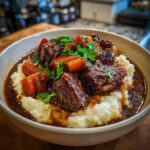 A bowl of tender apple cider beef stew served over creamy mashed potatoes, garnished with fresh parsley.