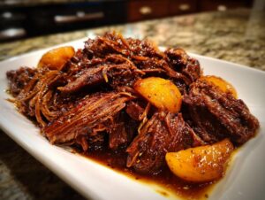 Close-up of tender Apple Cider Braised Pork Shoulder served with golden, spiced apple slices on a white platter.