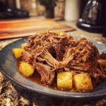 A plate of tender apple cider braised pork shoulder served with cubed potatoes in a rich sauce.