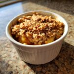 A close-up of a warm apple crisp served in a white ramekin, topped with a golden brown crumble.