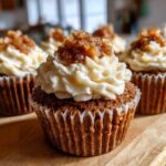 Close-up of a freshly baked apple pie cupcake topped with creamy white frosting and a sprinkle of cinnamon sugar.