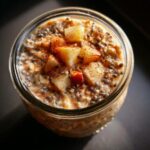 Overhead view of apple pie overnight oats in a glass jar, topped with diced apples and cinnamon.