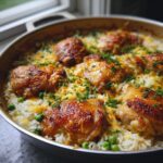 Close-up of a pan filled with golden brown baked chicken and rice, topped with melted cheese and fresh parsley.