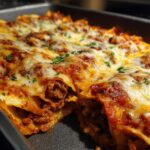 Close-up of baked beef enchiladas in a pan, covered in melted cheese and red sauce, sprinkled with parsley.