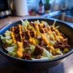 A close-up of a Big Mac salad in a black bowl, featuring lettuce, seasoned ground beef, pickles, onions, and a drizzle of special sauce.