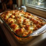 A golden-brown, bubbling broccoli cheese casserole in a glass baking dish, topped with herbs.