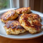 Close-up of golden brown canned salmon patties stacked on a white plate, ready to be served.