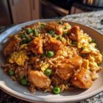 Close-up of a plate of chicken fried rice, featuring tender chicken pieces, bright green peas, and scrambled egg.