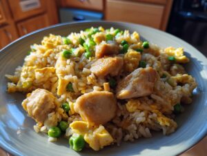 A close-up of a plate of homemade chicken fried rice, featuring tender chicken pieces, fluffy rice, scrambled egg, and bright green peas.