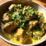 A close-up of creamy coconut chicken curry, garnished with fresh cilantro and red chili flakes.