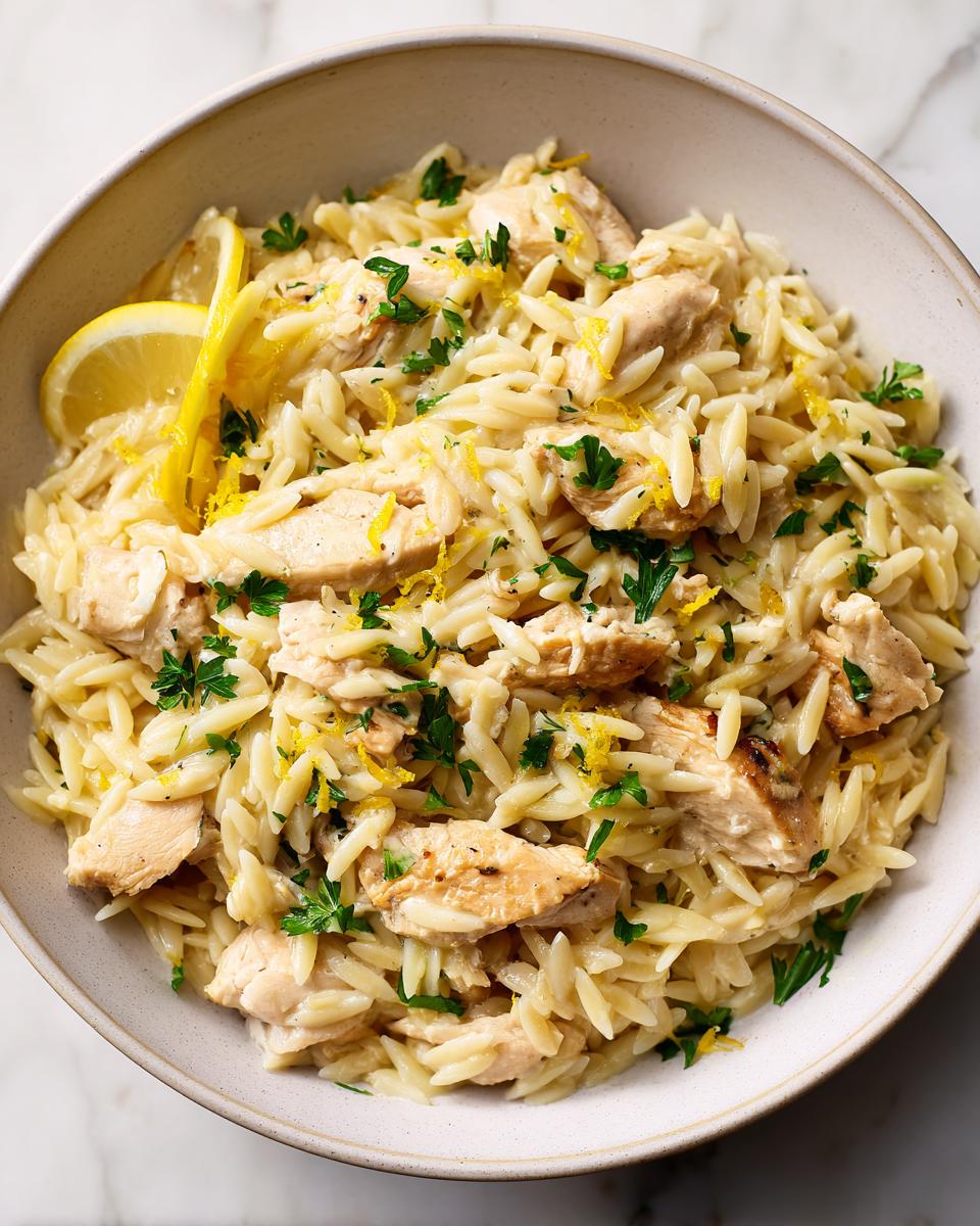 A bowl of creamy lemon chicken orzo topped with fresh parsley and lemon zest.
