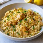 A close-up of a bowl filled with creamy lemon chicken orzo, garnished with lemon zest and parsley.
